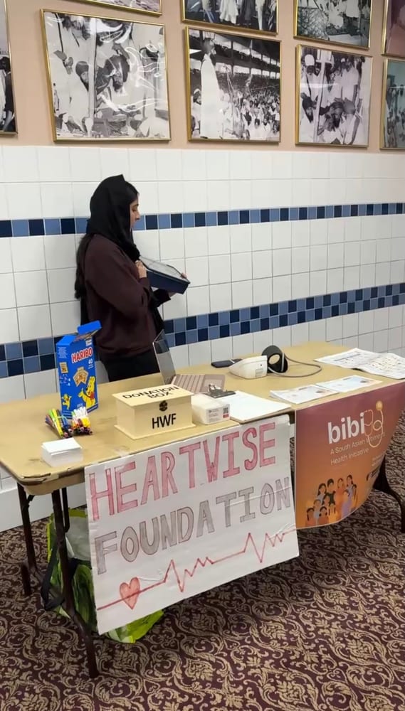 The HeartWise information table in a gurdwara hall with a hand-lettered poster, pamphlets and a partner banner.